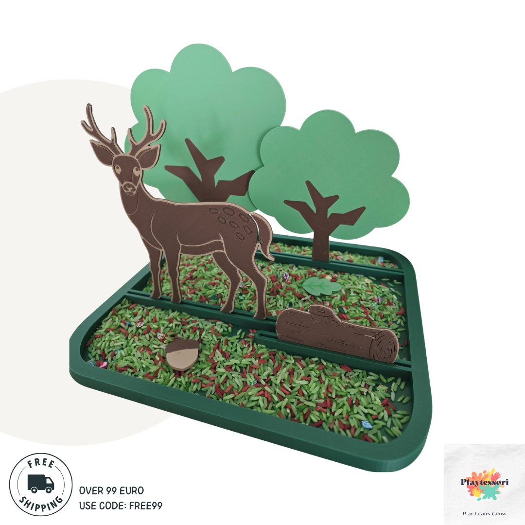 A forest-themed sensory play tray designed for children, featuring a 3D scene with a brown deer, three green trees, a wooden log, an acorn, and colorful rice representing grass and forest floor. The tray is sectioned and bordered in green plastic.