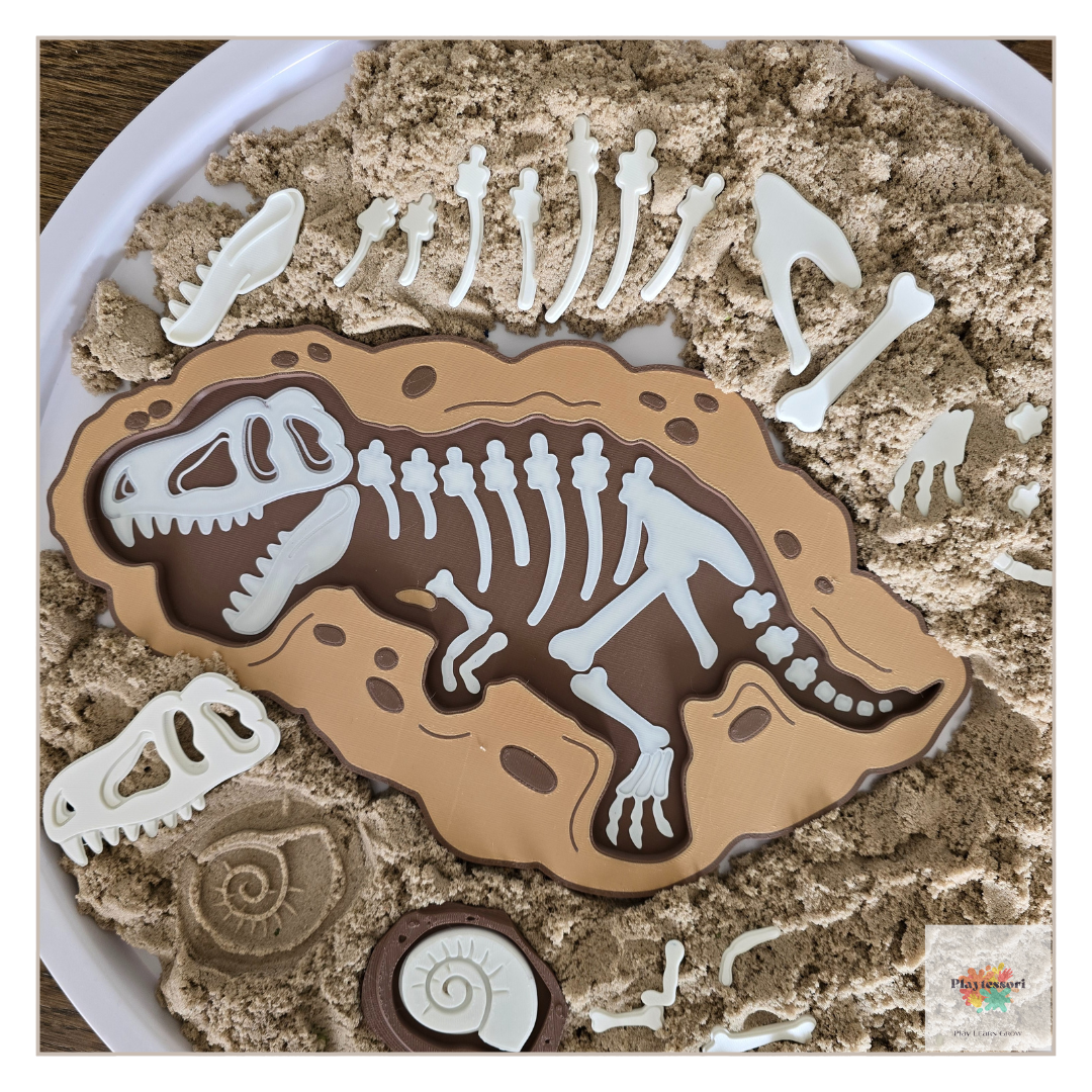 An overhead view of a dinosaur-themed sensory tray. A large, brown, 3D-printed tray with a white T-rex skeleton is nestled in beige sensory sand, surrounded by separate white fossil pieces.