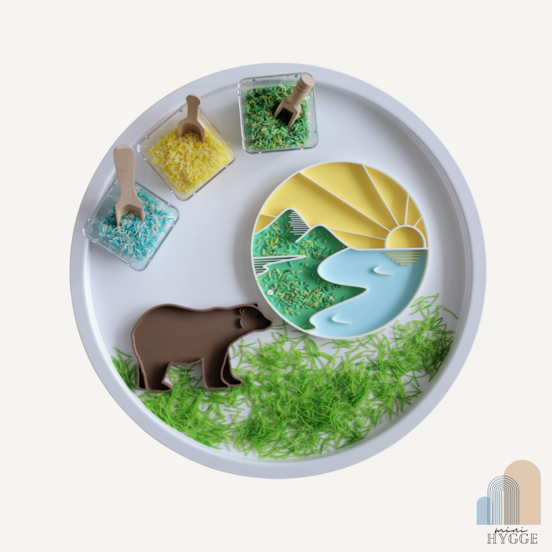 Sensorisch tray in zonsondergangthema met bergen en rivier, gevuld met gekleurde rijst – ideaal voor Montessori spel en natuurthema’s.