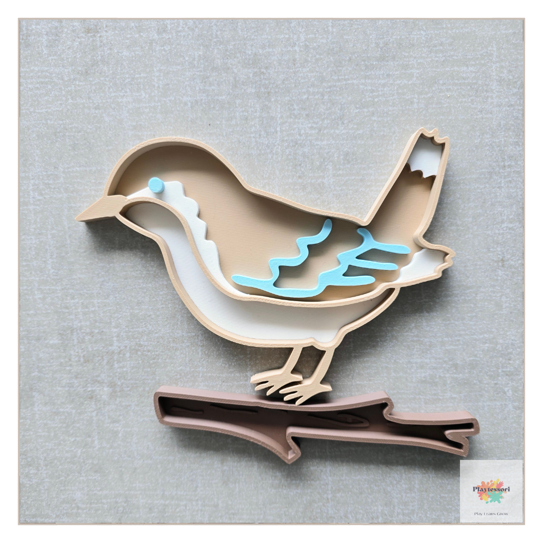 A beige, 3D-printed bird bio sensory tray with removable pieces, including a white belly, a light blue wing, and a separate brown branch piece for the bird to stand on.