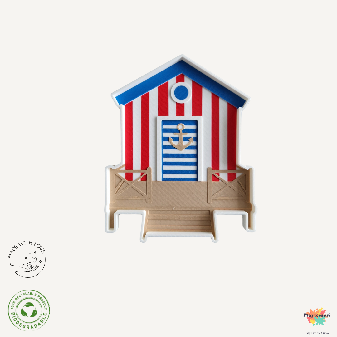 Sensorische speeltray in de vorm van een rood-wit strandhuis met blauwe details en anker op de deur – ideaal voor zomers zintuiglijk spel en boeiende speelsetups.