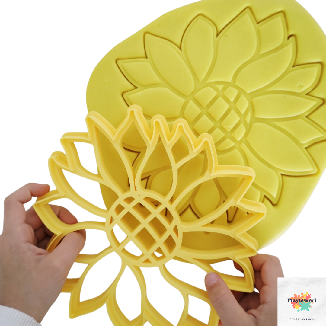 Kinderhanden houden een gele XL zonnebloem uitsteker vast, klaar om een afdruk te maken in gele playdough. Een tweede zonnebloemafdruk is al zichtbaar in de playdough