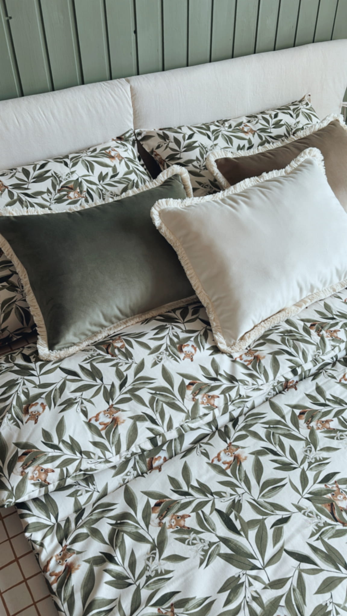 Slaapkamerset Woodland met dekbedovertrek met eekhoorns en bladeren, gecombineerd met decoratieve fluwelen kussens op een opgemaakt bed.