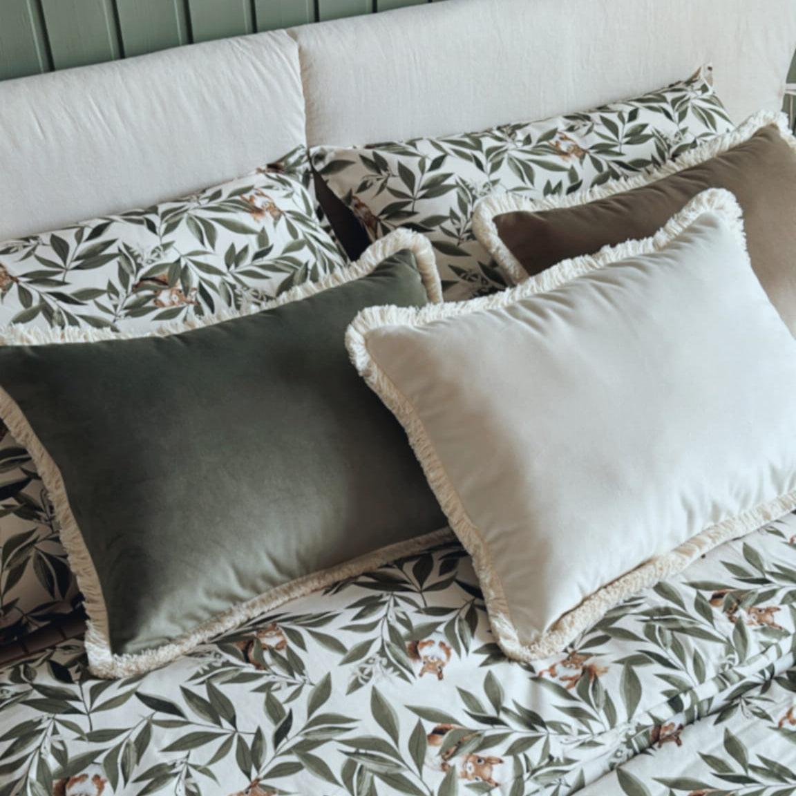 Slaapkamerset Woodland met dekbedovertrek met eekhoorns en bladeren, gecombineerd met decoratieve fluwelen kussens op een opgemaakt bed.