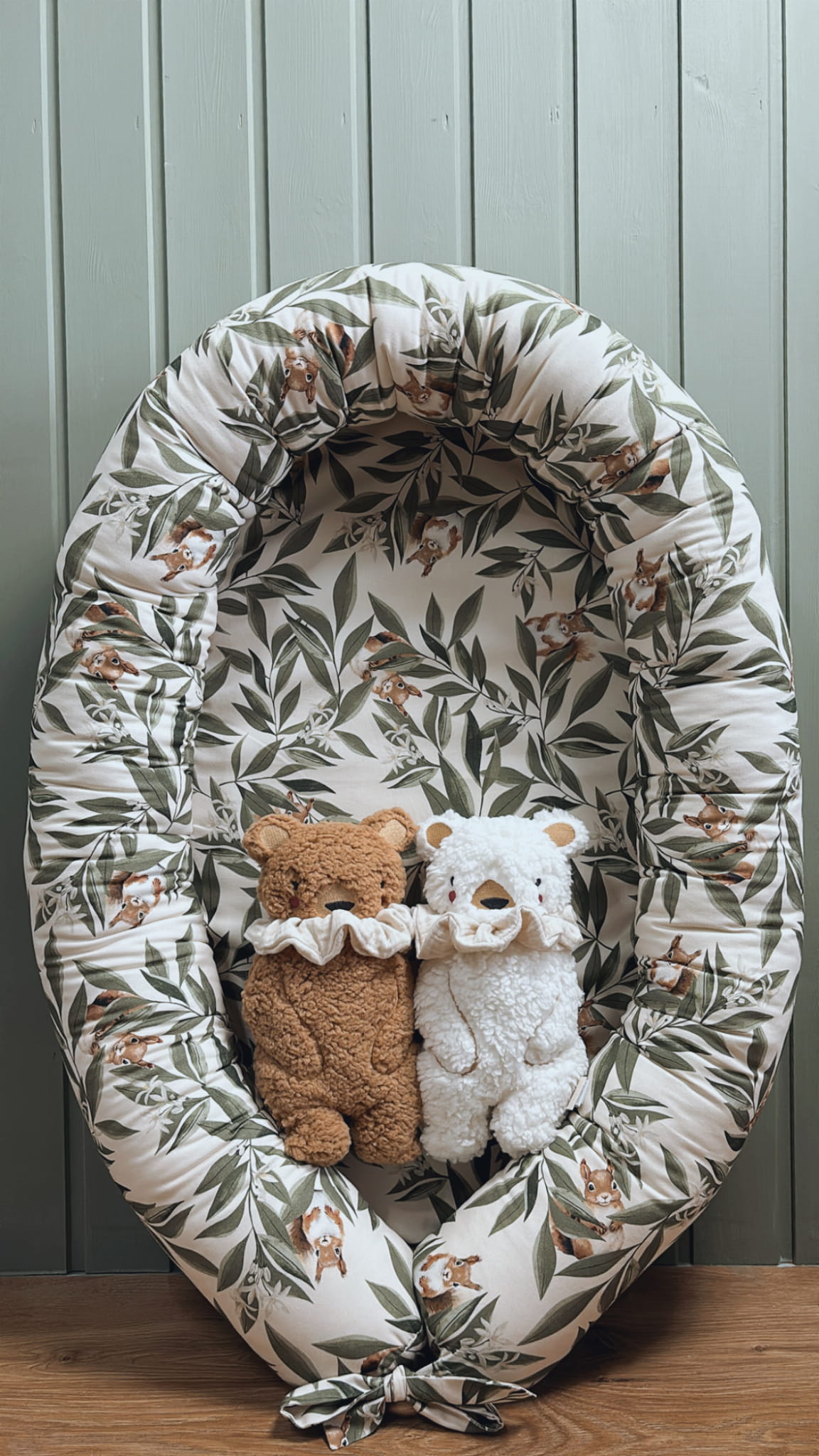 Babynestje met woodlandprint – blaadjes en eekhoorns – met daarin twee knuffelberen, een bruine en een witte, beide met een sierlijke kraag. Nestje staat op een houten vloer tegen een mintgroene houten wand.