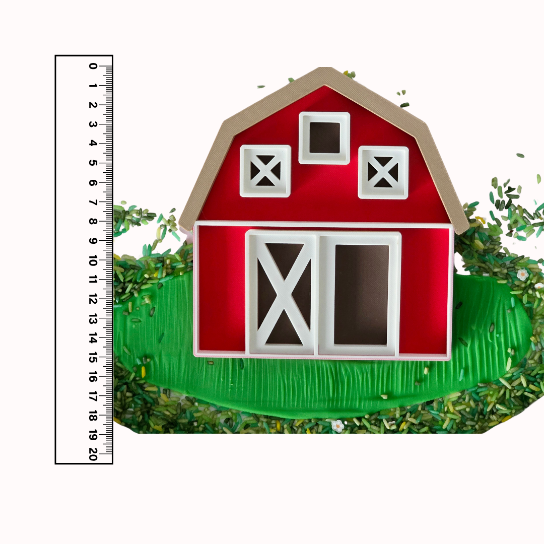 Ein 3D-gedrucktes sensorisches Spieltablett in Form einer roten Scheune mit weißen Fenster- und Türöffnungen sowie einem braunen Dach. Das Spieltablett besteht aus biologisch abbaubarem PLA und ist mit grünem und natürlich gefärbtem Reis als sensorisches Material gefüllt. Dieses pädagogische Spielzeug fördert kreatives und thematisches Spielen, perfekt für Bauernhof-Themen.