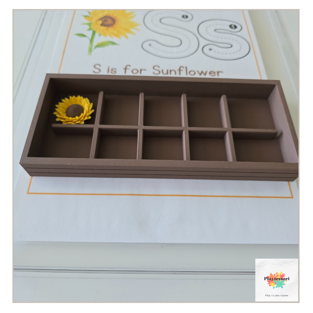 A close-up shot of the same brown, 3D-printed, rectangular tray with the removable grid insert removed. Three horizontal brown bars and three vertical brown bars are arranged in a large letter "S," placed on a piece of paper.
