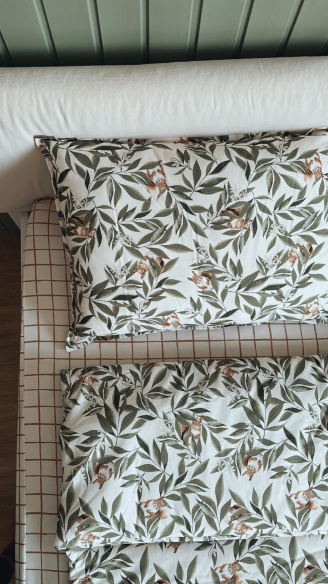 Kinderbeddenset uit de Woodland collectie met eekhoornmotief, bestaande uit een kussen en dekbed op een geruit hoeslaken in houten kinderbed.