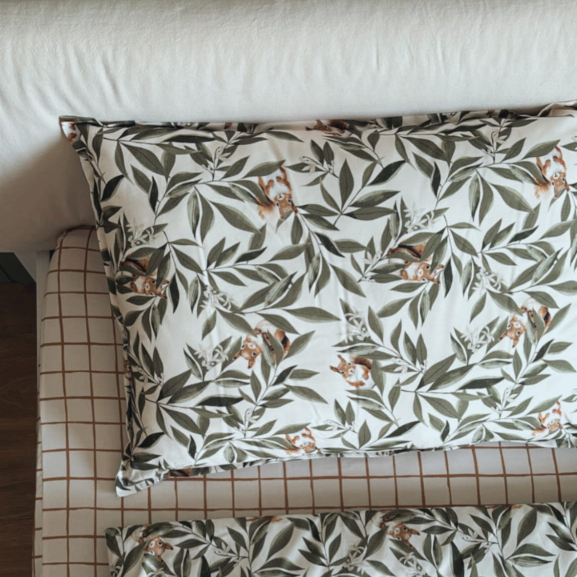 Kinderbeddenset uit de Woodland collectie met eekhoornmotief, bestaande uit een kussen en dekbed op een geruit hoeslaken in houten kinderbed.