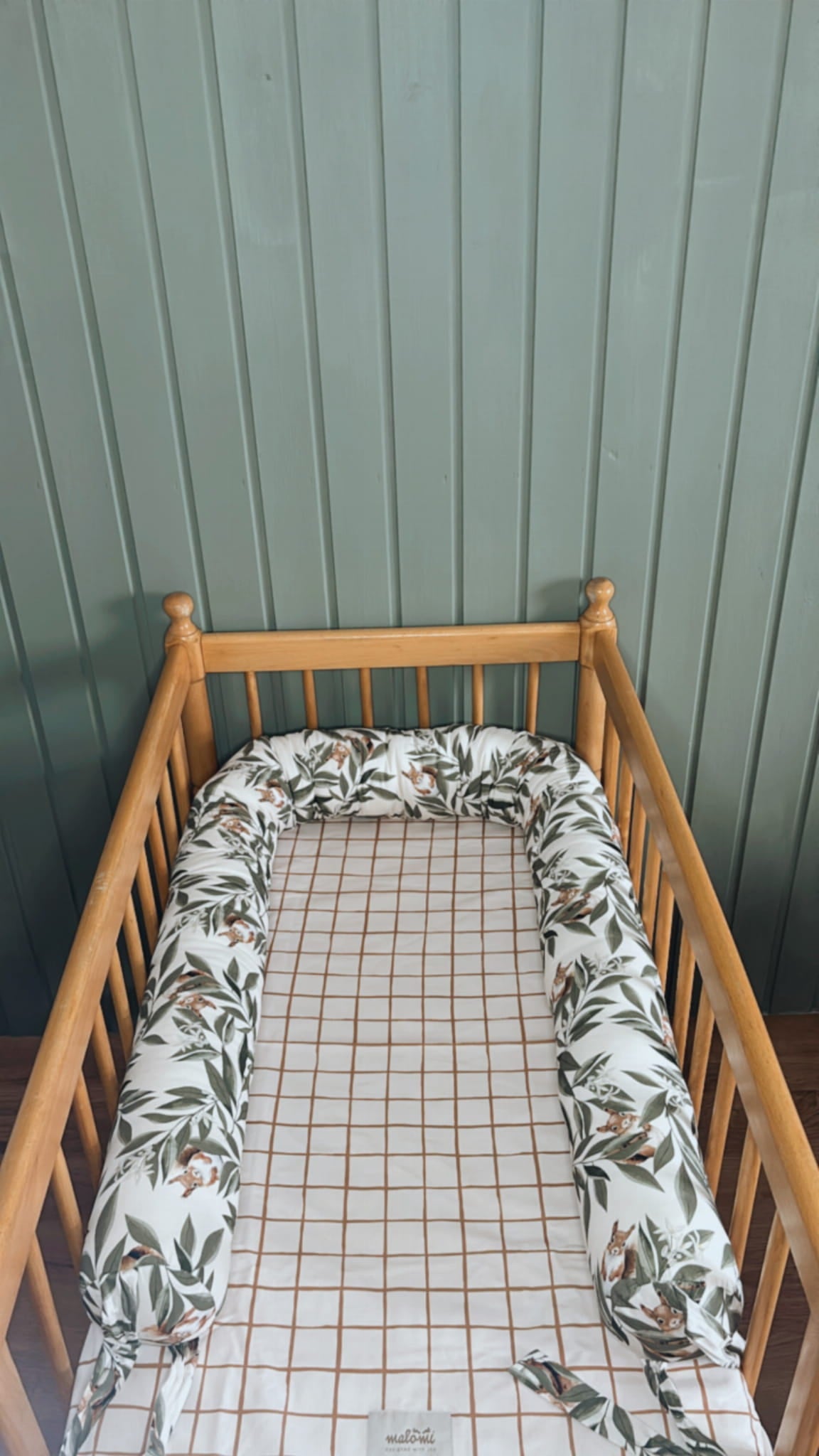 Open babynest met woodlandprint – blaadjes en eekhoorns – in een houten ledikantje met geruit hoeslaken en mintgroene houten muur op de achtergrond.
