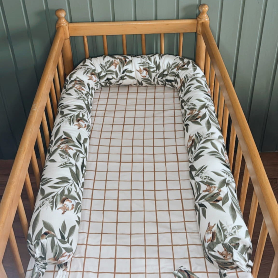 Open babynest met woodlandprint – blaadjes en eekhoorns – in een houten ledikantje met geruit hoeslaken en mintgroene houten muur op de achtergrond.