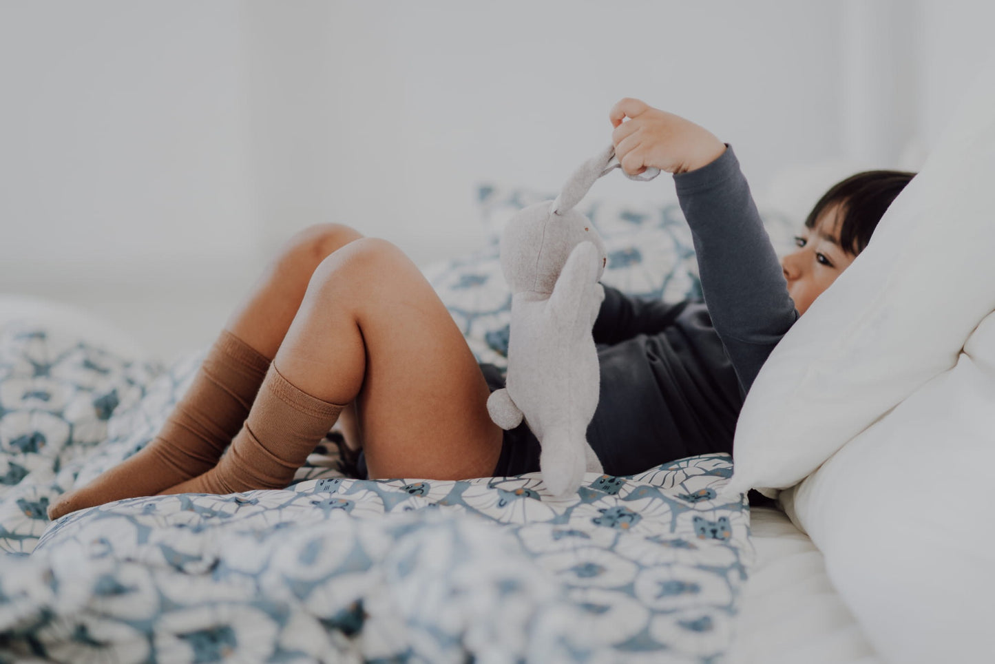 Kind speelt met knuffel op bed met denim leeuwenprint beddengoed.