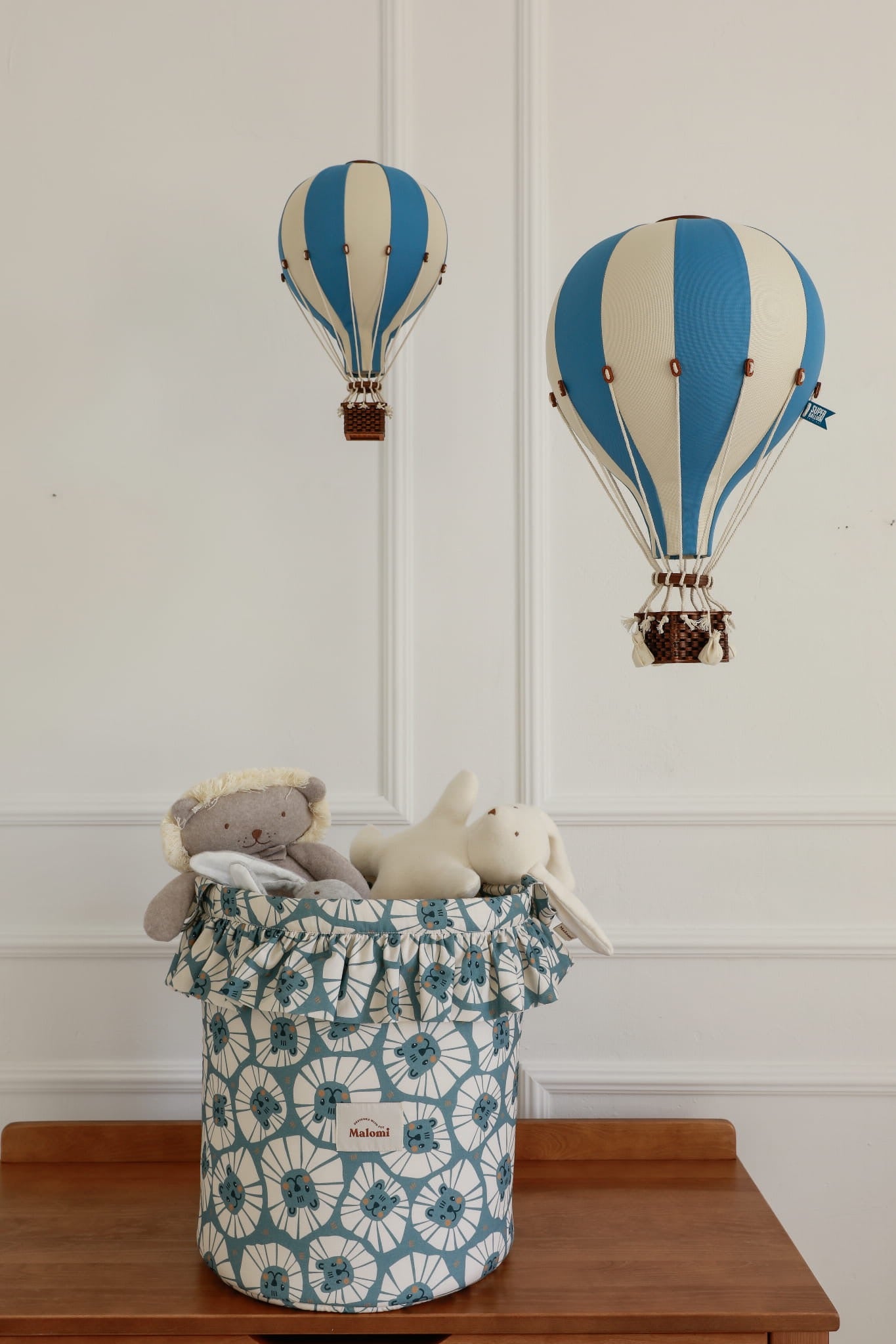 Speelgoedmand gevuld met knuffels, onder decoratieve blauwe luchtballonnen in kinderkamer