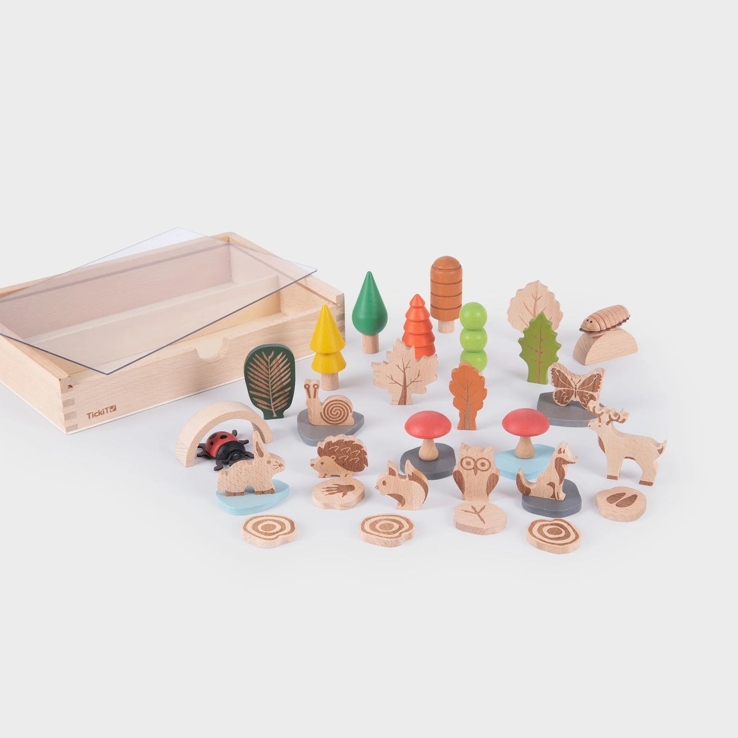 Uitgestalde TickiT Bospadenset met houten dieren, bladeren, paddenstoelen, bomen en accessoires op tafel naast de opbergdoos