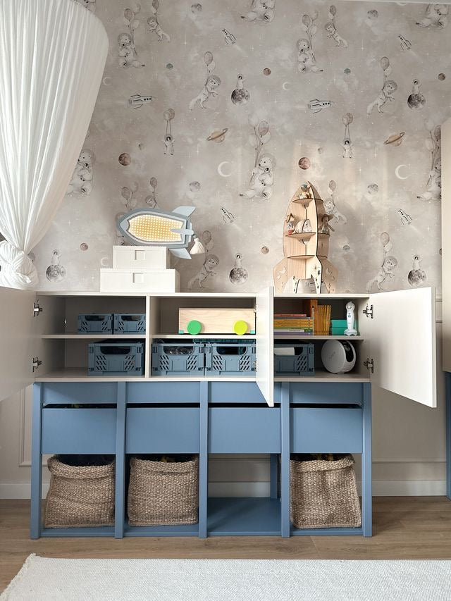 Wauw, kijk eens binnenin! Deze open Tweens commode in fris wit en zacht muted blauw toont zijn slimme opbergruimte met blauwe kratten en een houten doosje. De kinderkamer is prachtig versierd met een ruimte-thema behang en een zwevend wit gordijn.