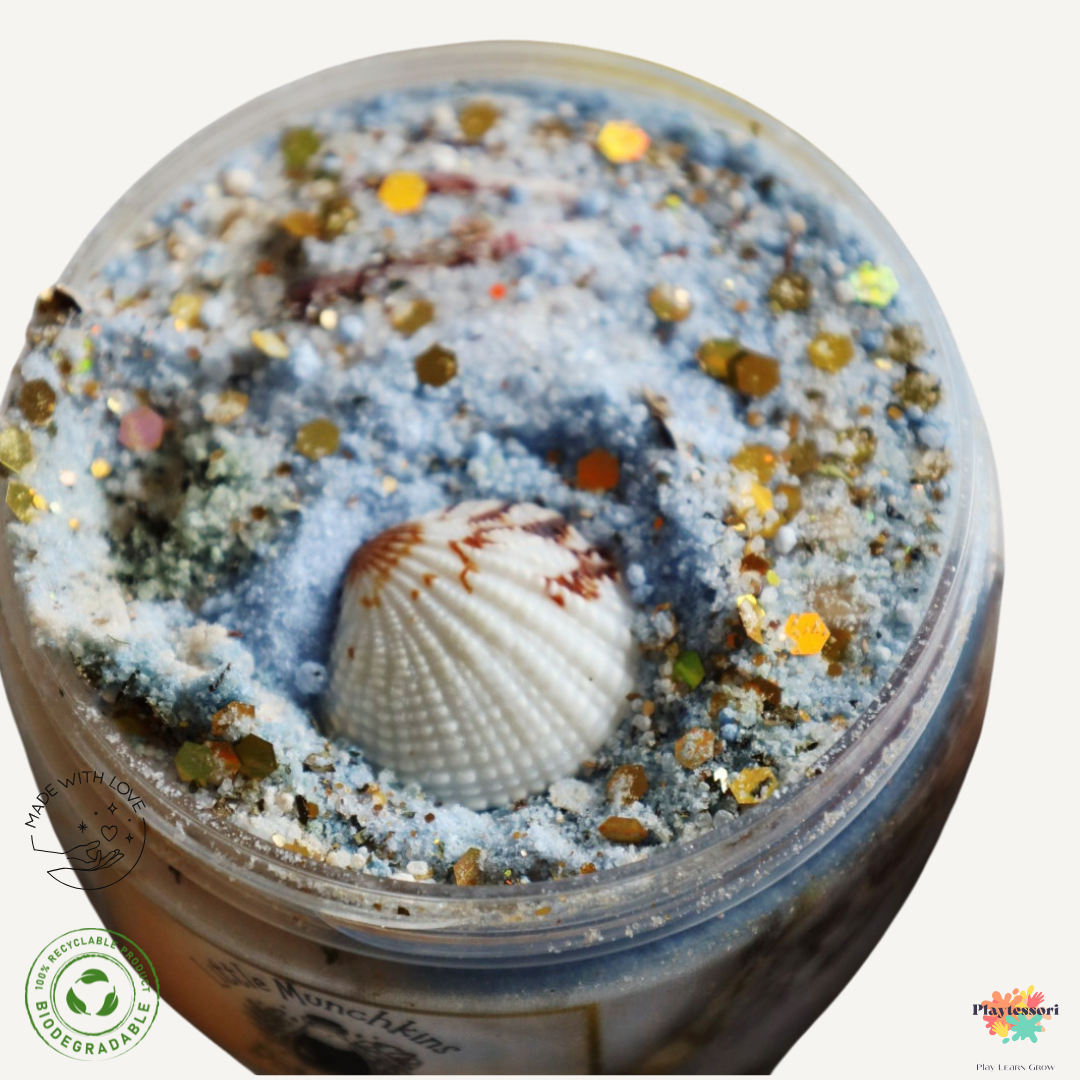 Een potje met de Bruisende Botanicals: Zee Schuim mix. De mix is blauw en geel en bevat echt zand, goudkleurige stenen en schelpen.