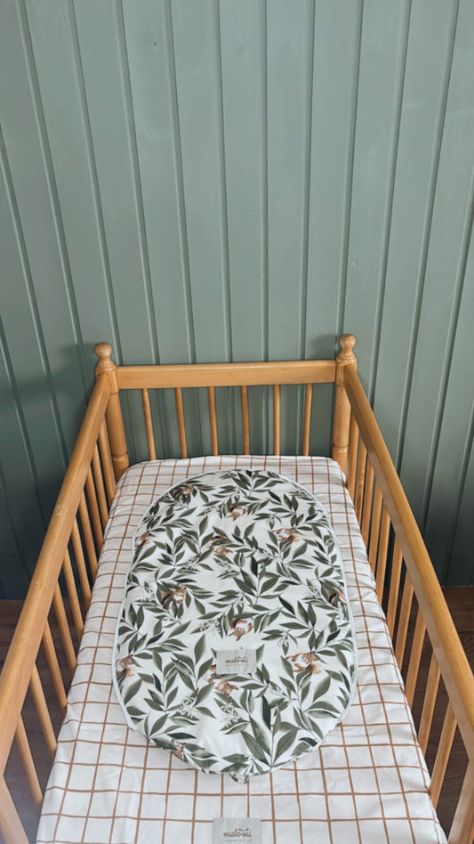 Babymatrasbeschermer met woodlandprint in een houten ledikantje met geruit hoeslaken. De beschermer is gemaakt van katoen en toont een speels motief van blaadjes en eekhoorns.