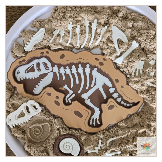 An overhead view of a dinosaur-themed sensory tray. A large, brown, 3D-printed tray with a white T-rex skeleton is nestled in beige sensory sand, surrounded by separate white fossil pieces.