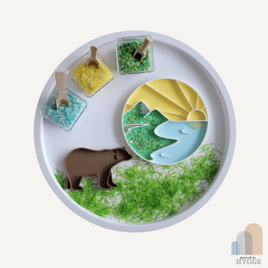 Sensorisch tray in zonsondergangthema met bergen en rivier, gevuld met gekleurde rijst – ideaal voor Montessori spel en natuurthema’s.