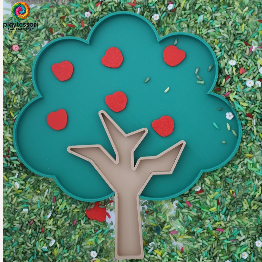 Groene sensorische speeltray in de vorm van een boom, omringd door groen speelrijst en rode appeltjes. Ideaal voor montessori-activiteiten en themaspel.