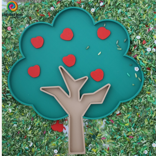 Groene sensorische speeltray in de vorm van een boom, omringd door groen speelrijst en rode appeltjes. Ideaal voor montessori-activiteiten en themaspel.