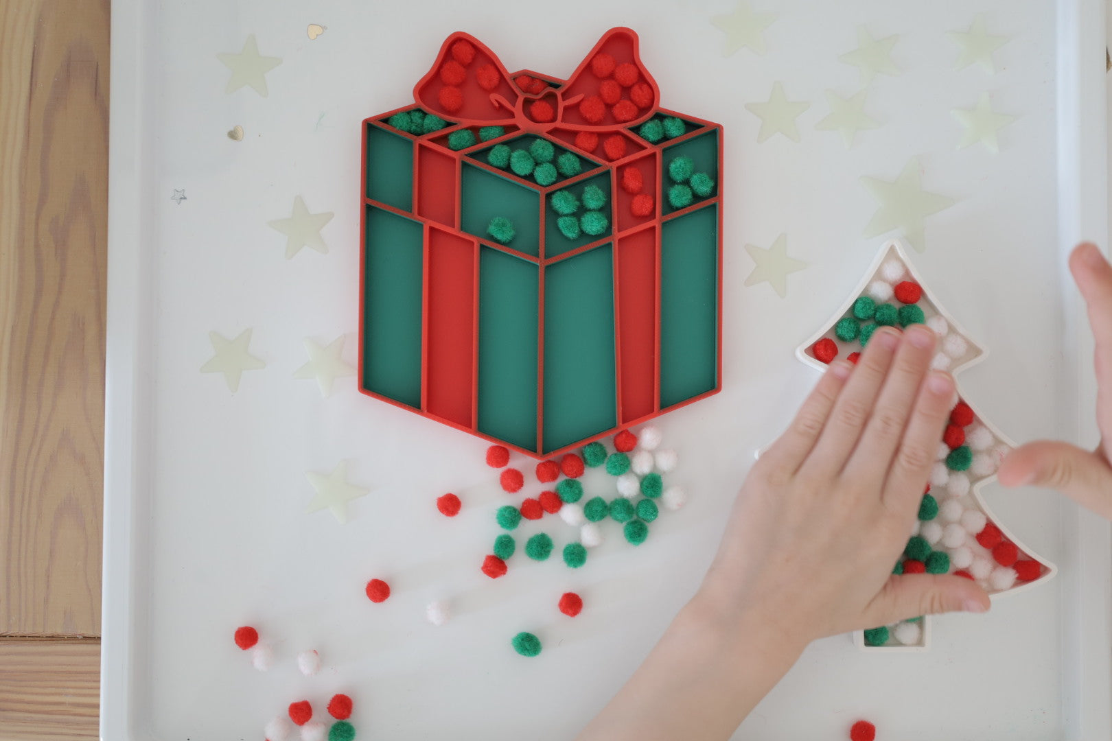 Christmas-themed 3D-printed sensory tray, featuring a festive gift box and tree design, filled with red, green, and white pom-poms for sensory play.