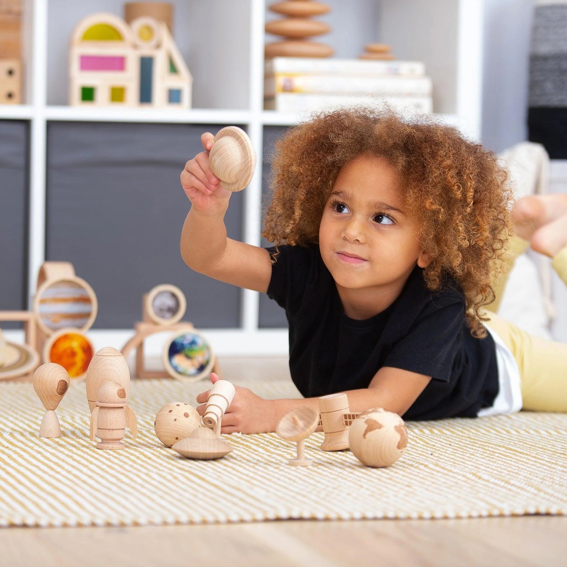 Kind speelt met houten ruimtefiguren van TickiT®, houdt een planeet omhoog tijdens fantasierijk en educatief rollenspel.