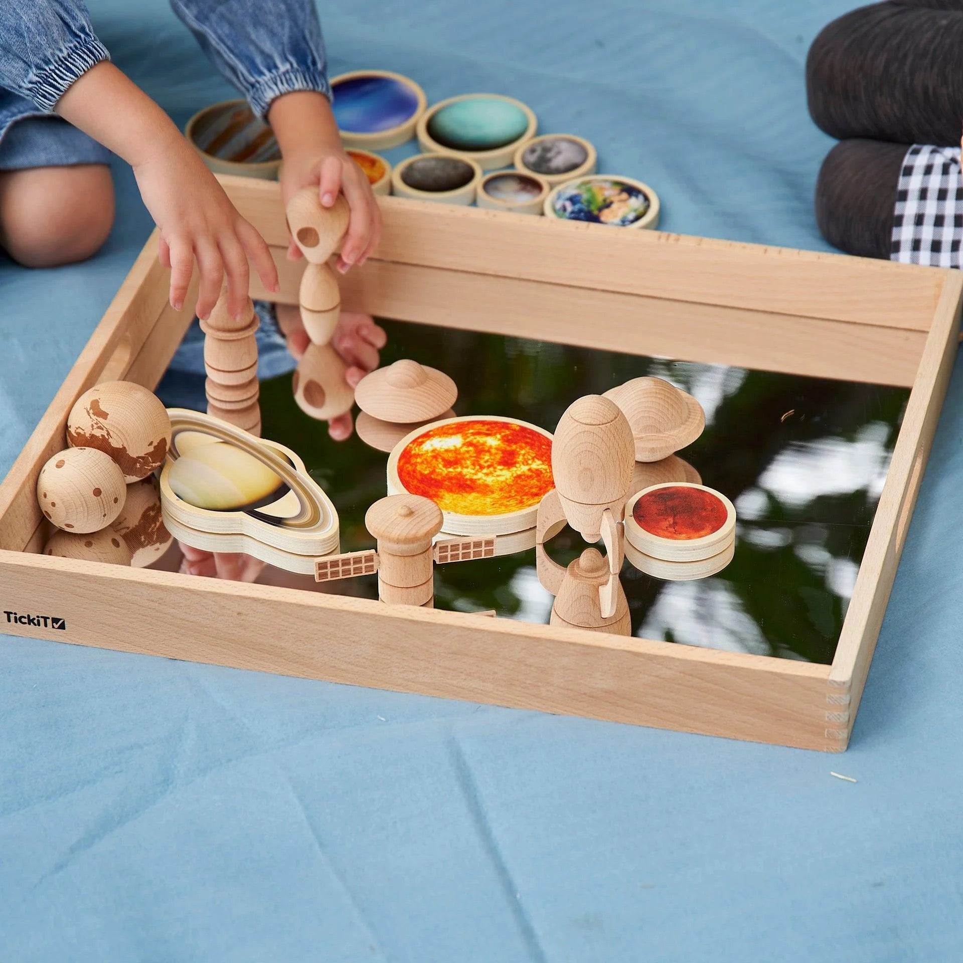 Kinderen spelen met de houten ruimteavontuurset op een spiegeltray, gecombineerd met planetenschijven voor een zintuiglijke en fantasierijke leerervaring.
